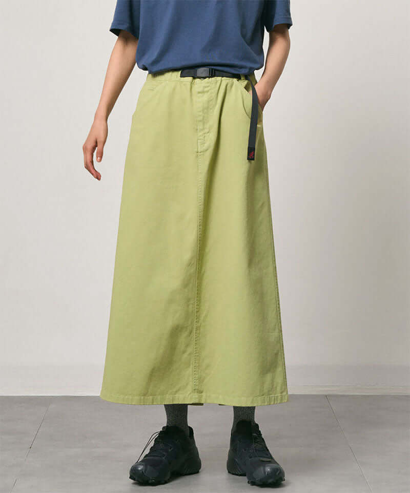 Model wearing a elm pigment colored Gramicci 5-Pocket Skirt and a blue shirt on a light-tone background.