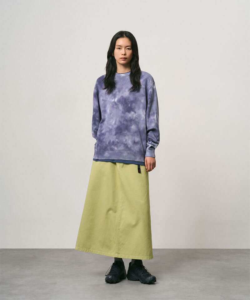 Model wearing a elm pigment colored Gramicci 5-Pocket Skirt and a purple tie-dye sweatshirt on a light-tone background.