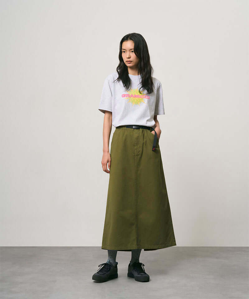 Model wearing a olive colored Gramicci 5-Pocket Skirt and a white shirt on a light-tone background.