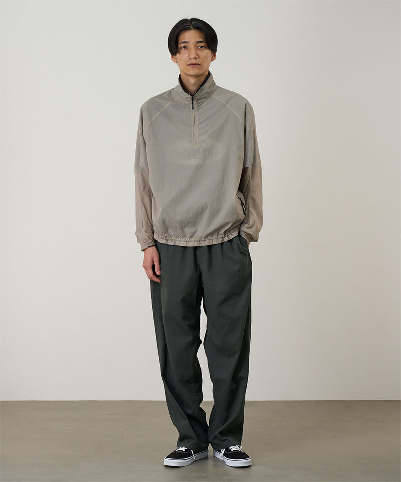 Model wearing a concrete colored Gramicci Ultra-Light Packable Jacket and dark grey pants on a light-tone background.