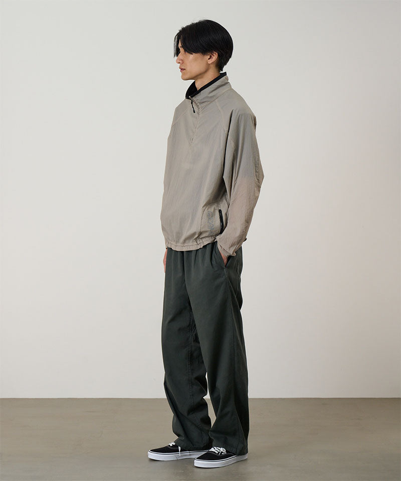 Model wearing a concrete colored Gramicci Ultra-Light Packable Jacket and dark grey pants on a light-tone background.