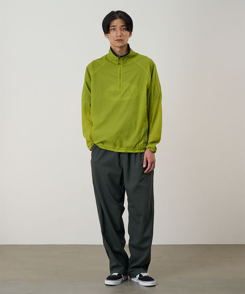 Model wearing a kiwi Gramicci Ultra-Light Packable Jacket and grey pants on a light-tone background.