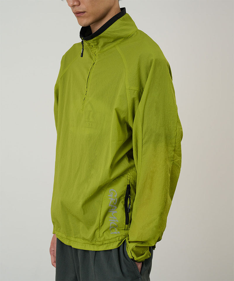 Model wearing a kiwi Gramicci Ultra-Light Packable Jacket against a light-tone background.