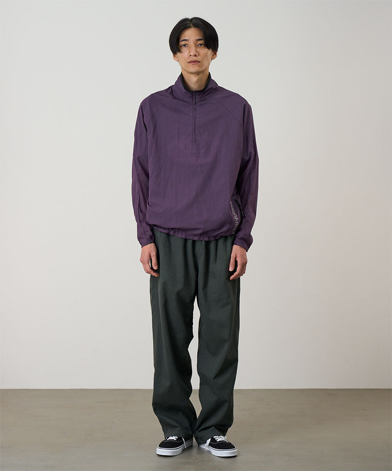 Model wearing a iris purple Gramicci Ultra-Light Packable Jacket and dark grey pants on a light-tone background.