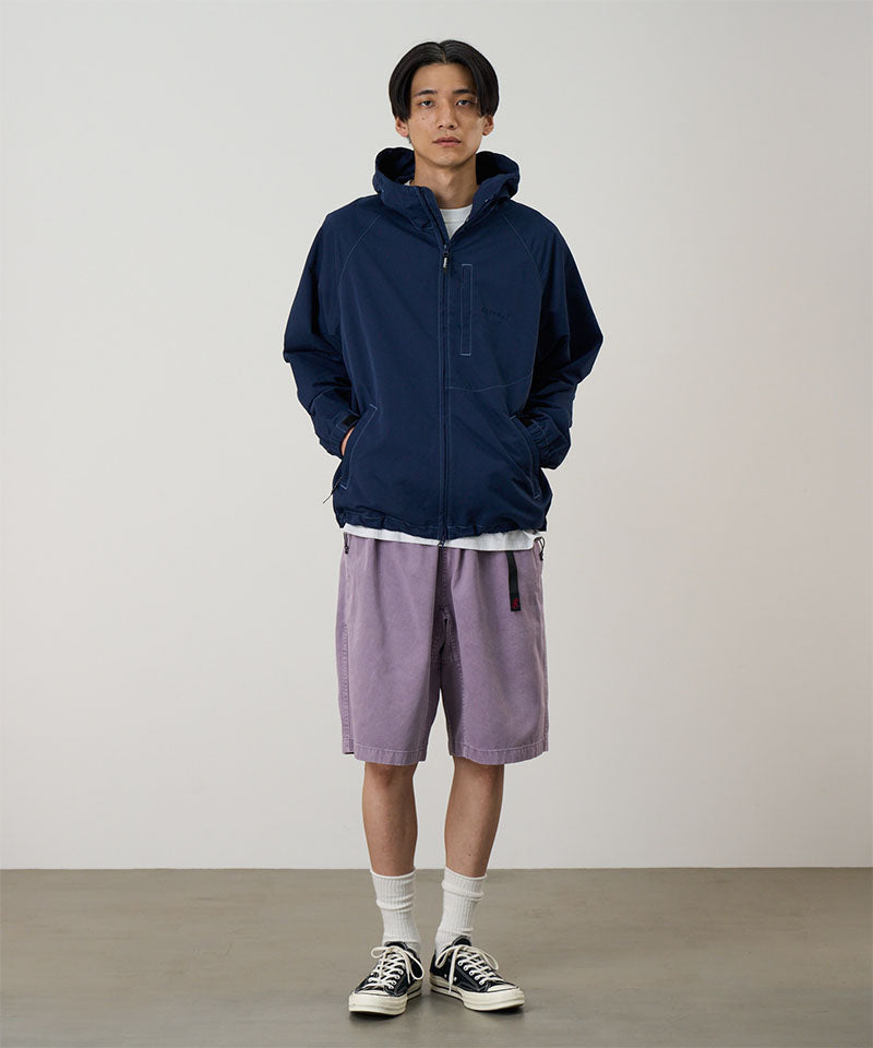 Model wearing a dark navy Gramicci Milton Hooded Jacket and purple shorts on a light-tone background.
