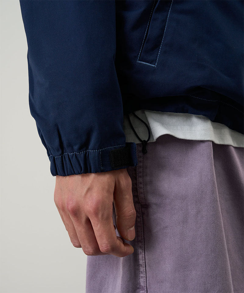 Model wearing a dark navy Gramicci Milton Hooded Jacket and purple shorts on a light-tone background.