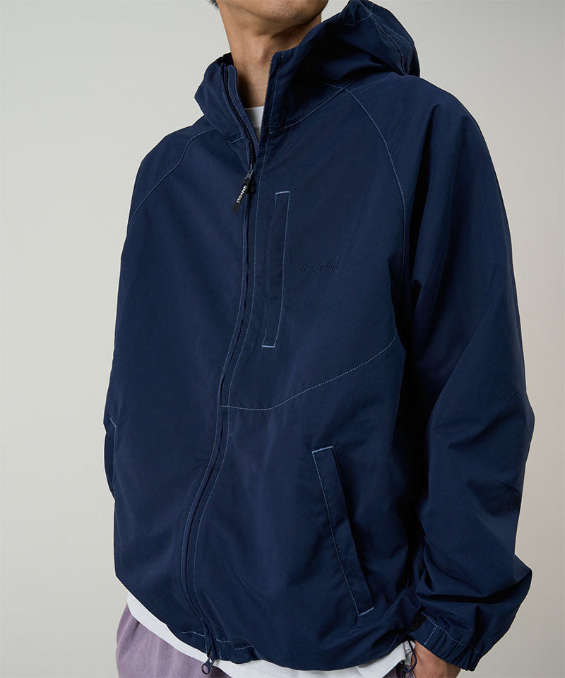Model wearing a Gramicci dark navy Milton Hooded Jacket against a light-tone background.