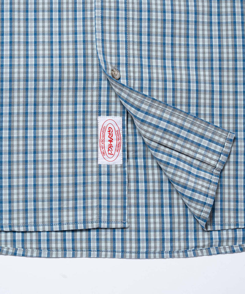 Close-up view of a Gramicci Poplin Millwood Shirt pocket in blue plaid on a light-tone background.