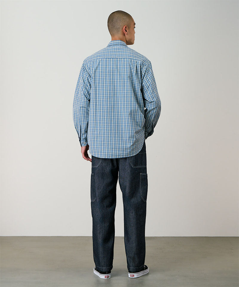 Back view of a model wearing a blue plaid Gramicci Poplin Millwood Shirt and blue pants on a light-tone background.