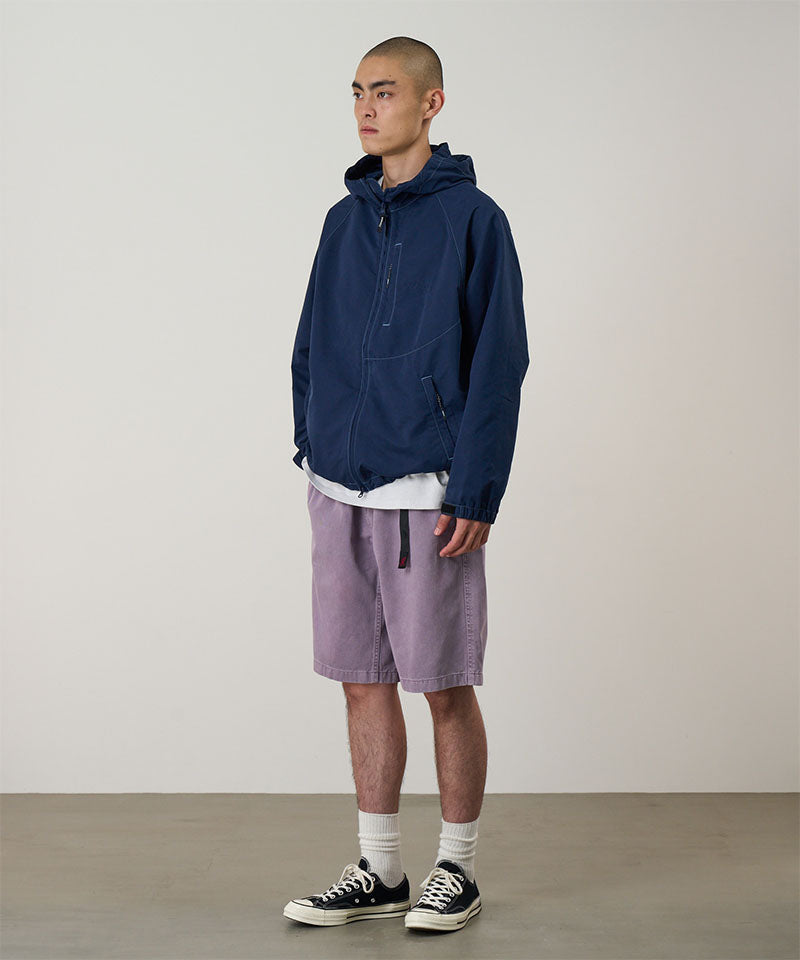 Model wearing a Gramicci Natural Dyed Jam Short in the color purple and a blue hoodie on a light-tone background.