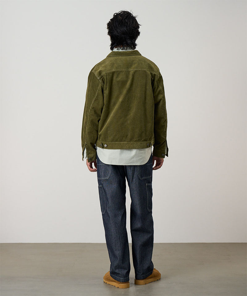 Back view of a model wearing navy Japanese Chambray Rock Slide Pants and a moss green jacket on a light-tone background.