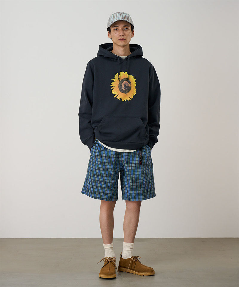 Model wearing a blue multistripe Gramicci Gramicci O.G. G-Short Seersucker Plaid with grey and green graphic and navy hoodie on a light-tone background.