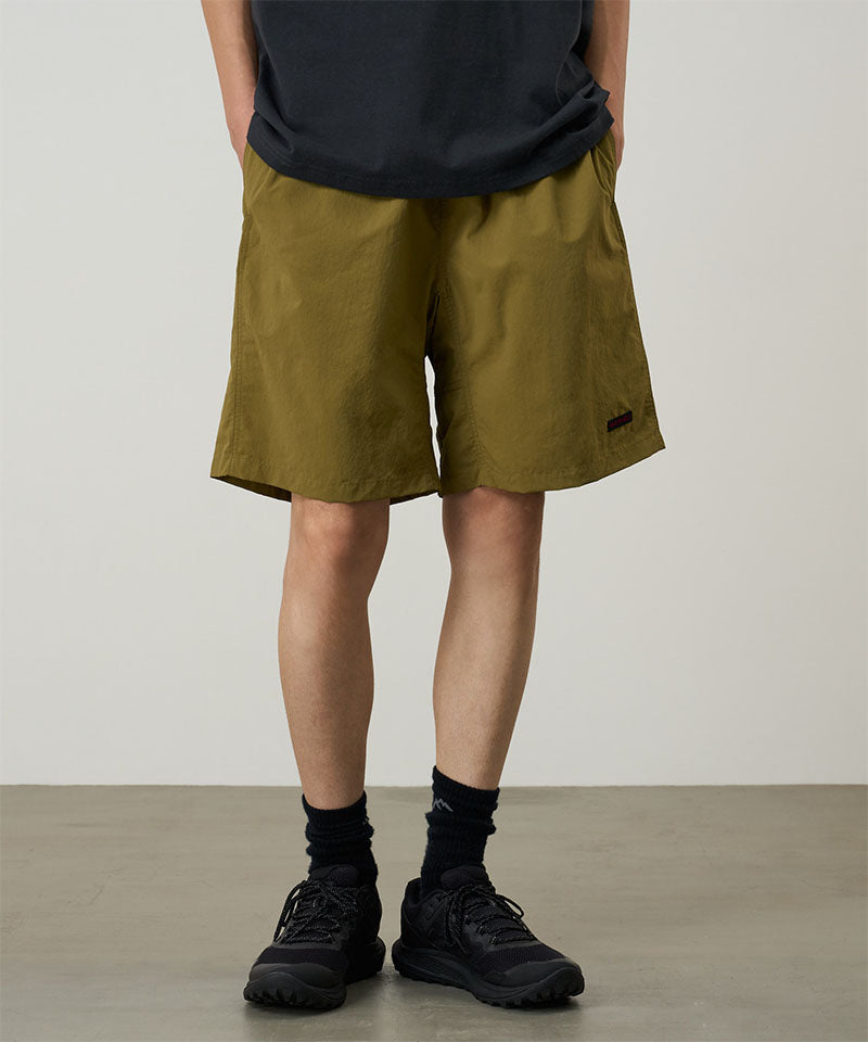 Person wearing olive green shorts and black shoes on a plain background
