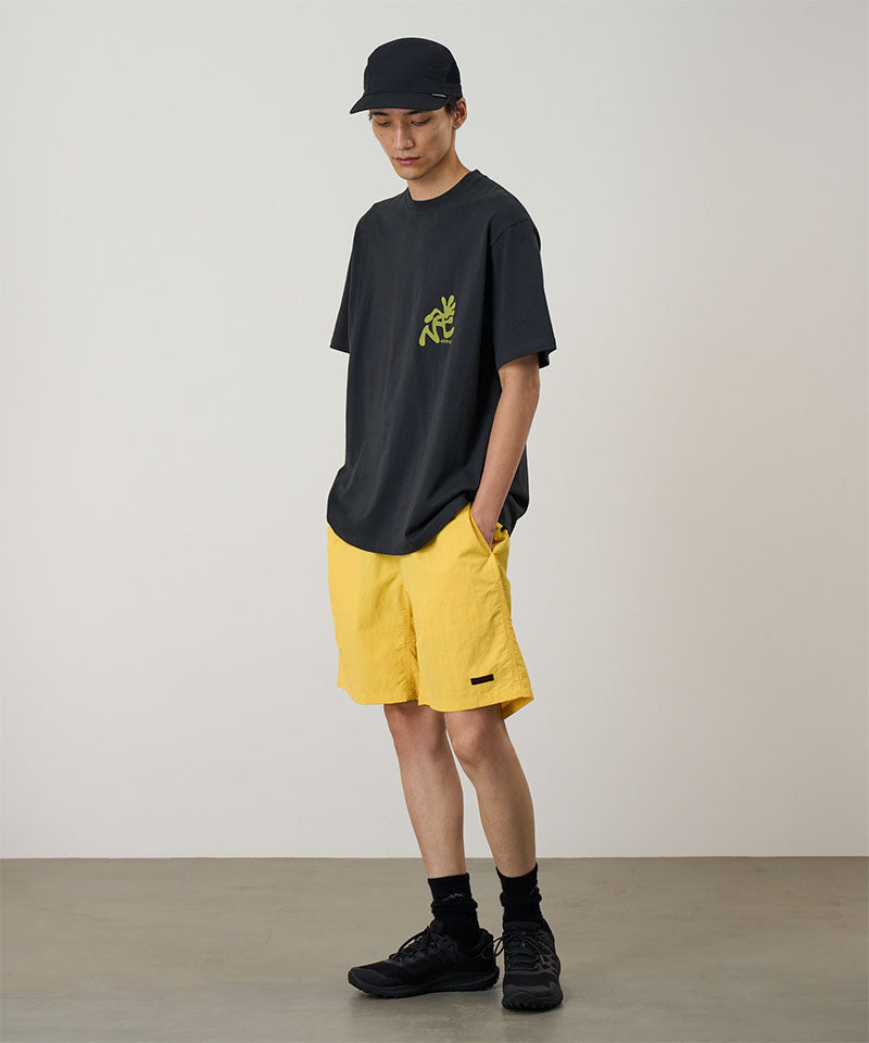 Person wearing a black t-shirt with a yellow logo and yellow shorts against a plain background