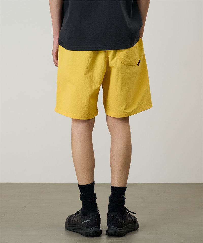 Person wearing yellow shorts and black shoes on a plain background