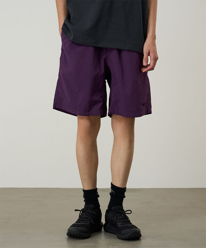 Person wearing purple shorts and black shoes on a plain background