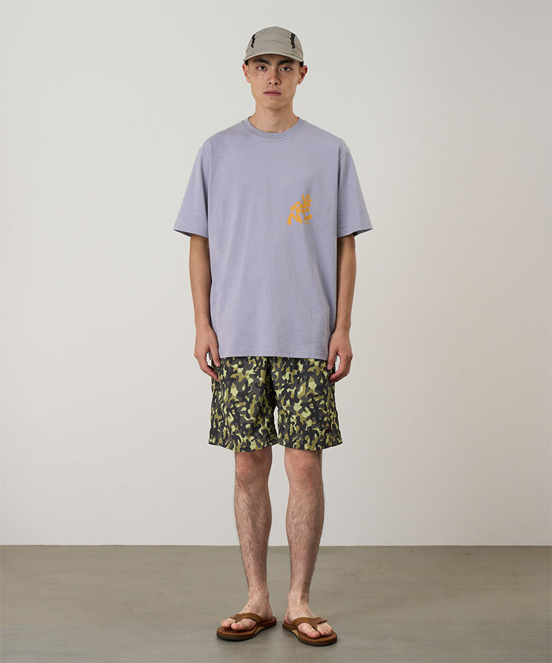 Person wearing a light purple t-shirt with a logo and camouflage shorts on a plain background