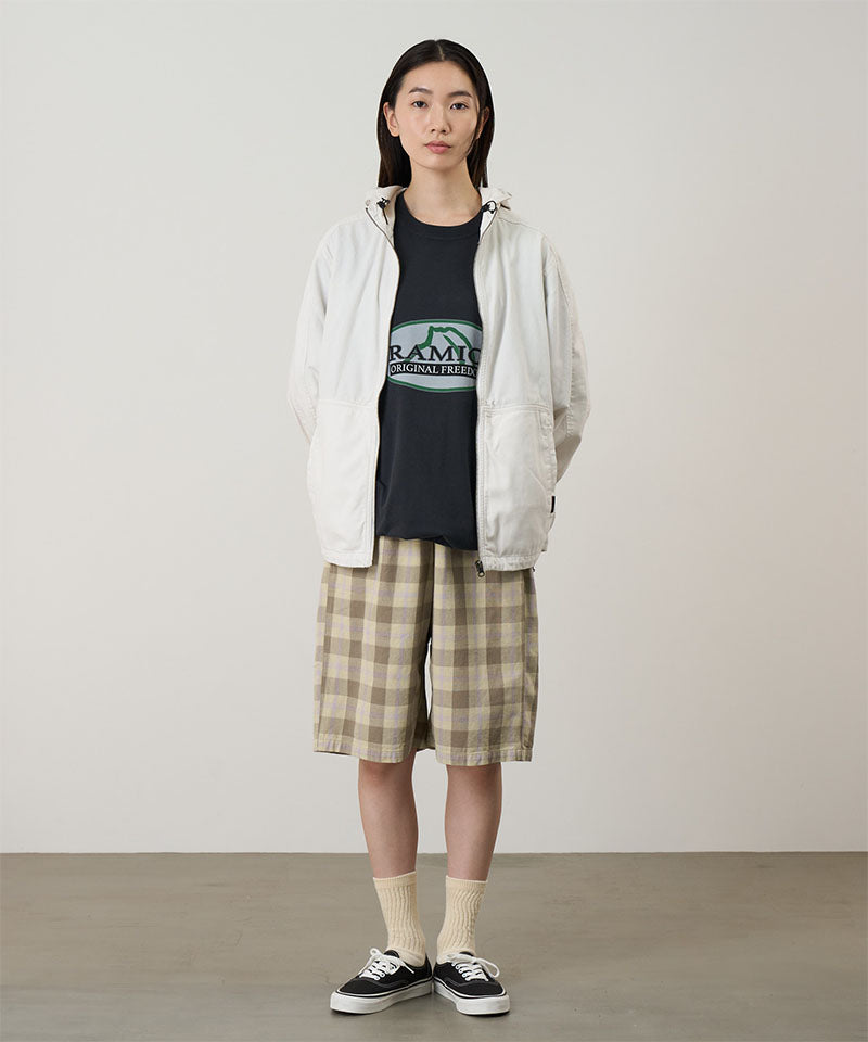 Model wearing the Gramicci Beach Hoodie Jacket in stone with tan plaid shorts on a light tone background.