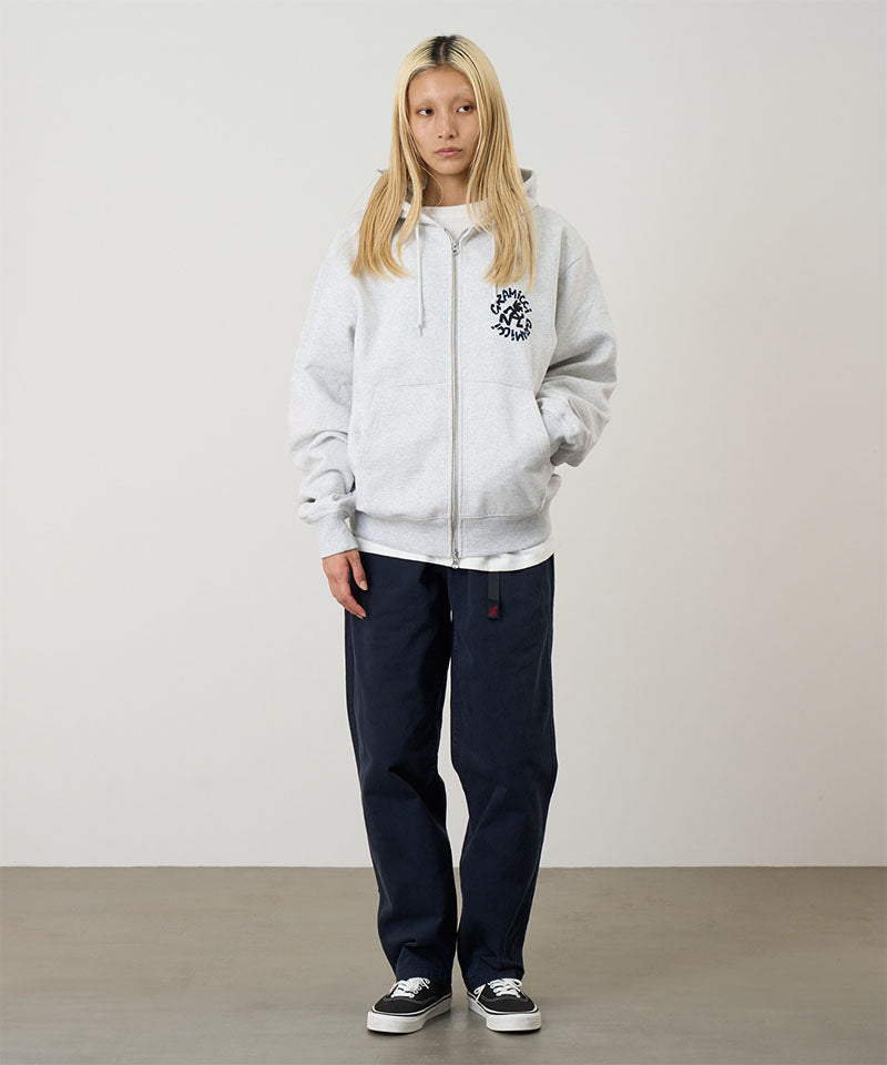 Model wearing heather ash Gramicci Running Man Zip Hooded Sweatshirt and a blue pants on a light-tone background.