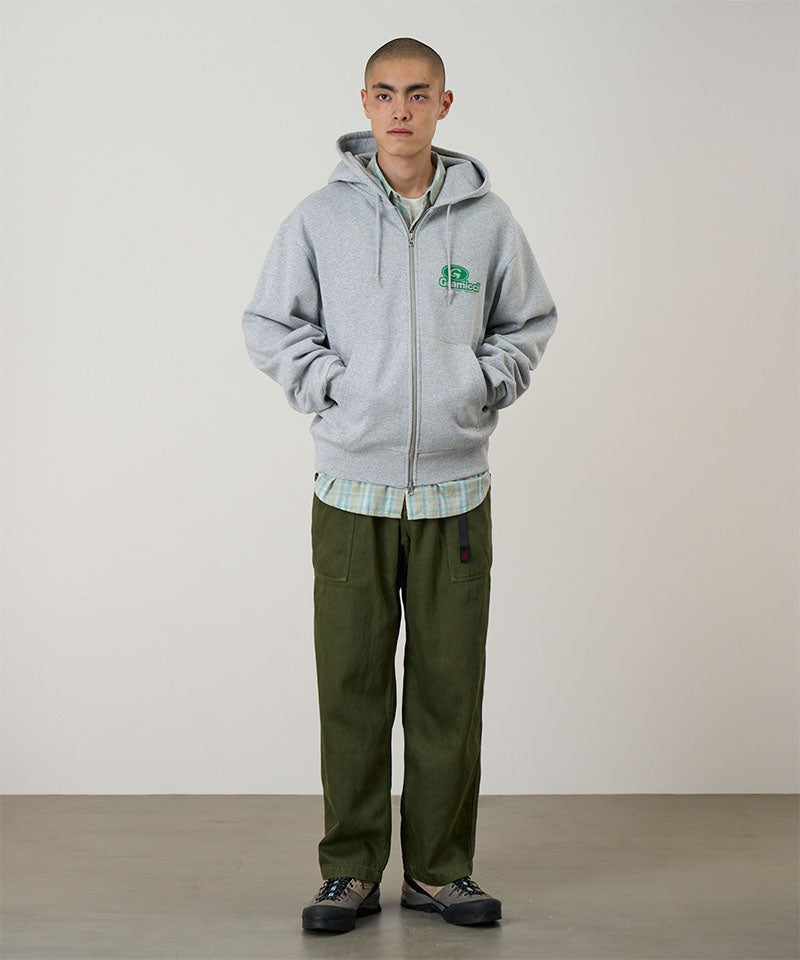 Person wearing a gray hoodie with a logo, plaid shirt, and green pants against a plain background