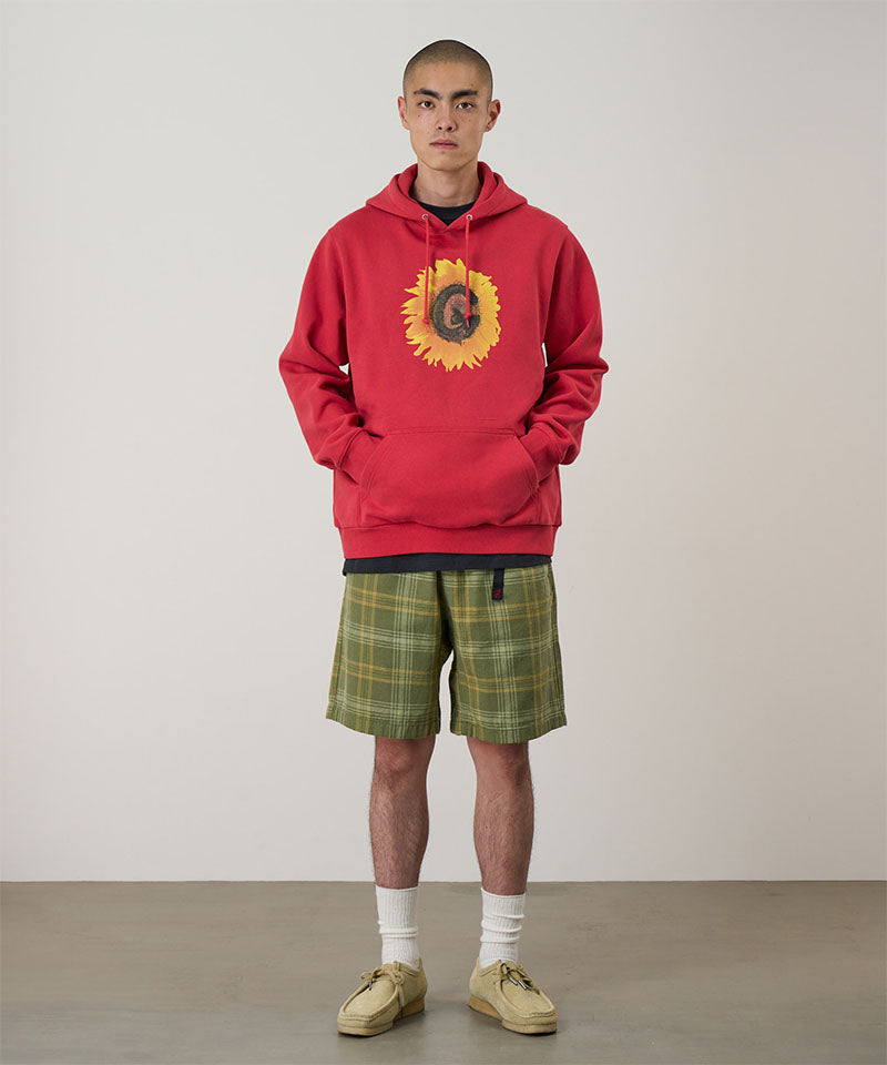 Person wearing a red hoodie with a sunflower design and plaid shorts on a plain background