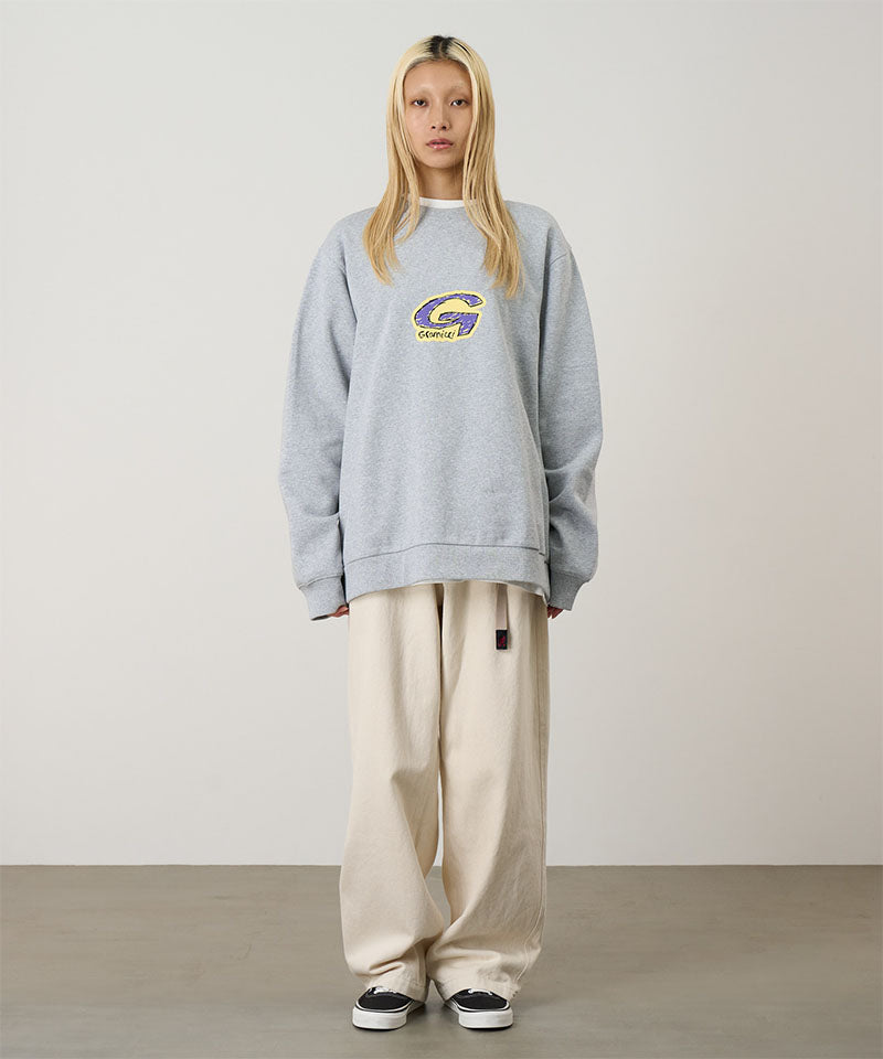 Person wearing a gray sweatshirt with a logo and beige pants on a plain background