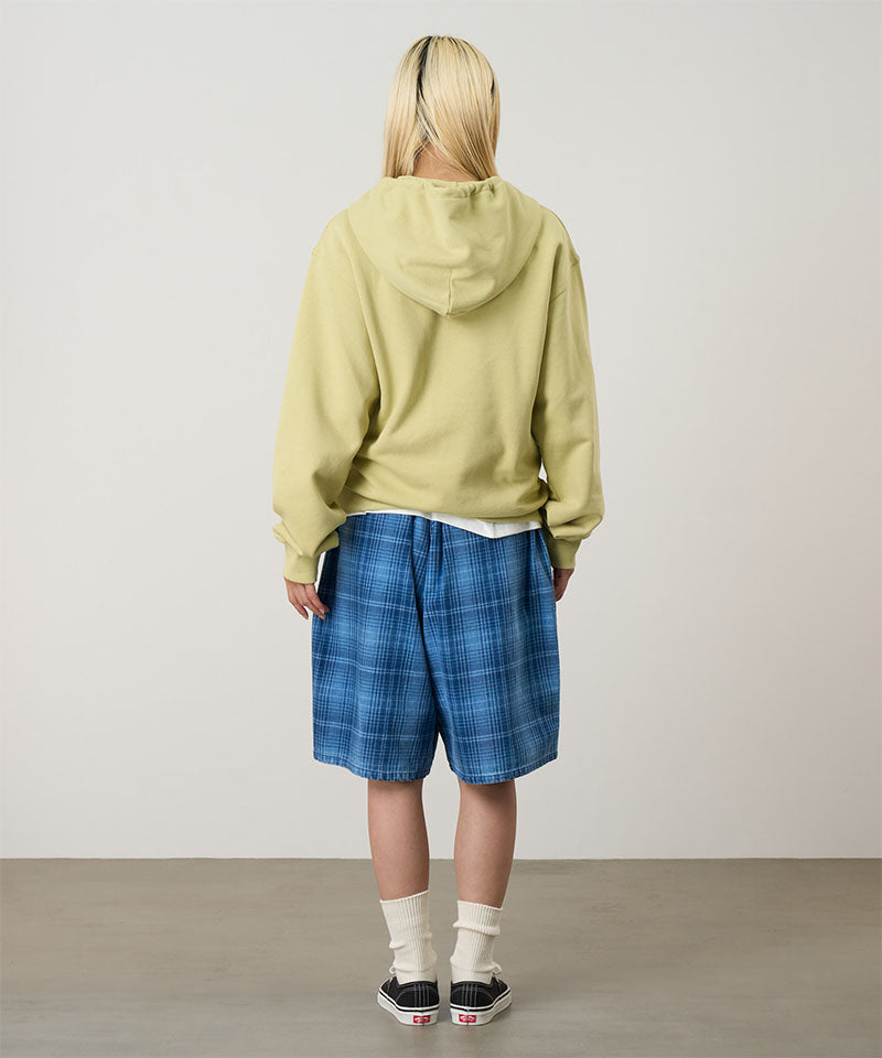 Person wearing a light green hoodie and blue plaid shorts standing against a plain background