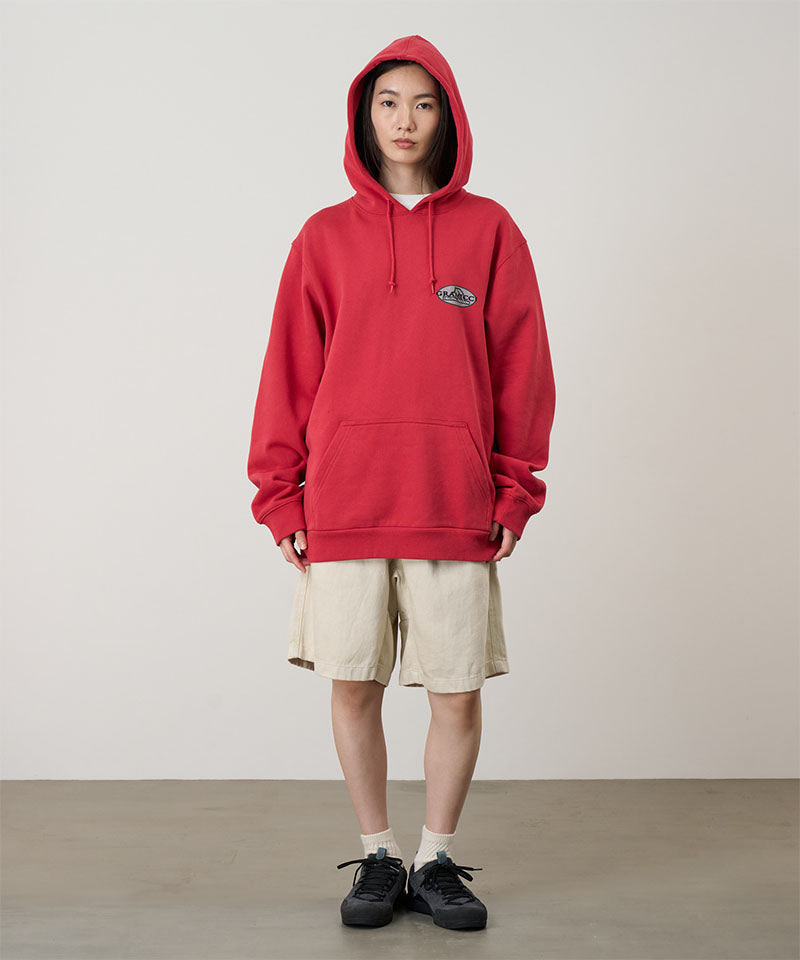 Person wearing a red hoodie with a logo, beige shorts, and black shoes on a plain background