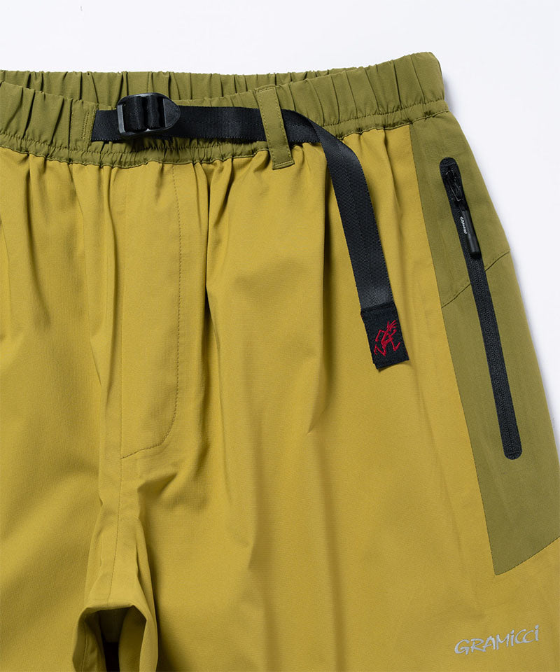 Olive yellow pants with a black zipper and logo on a light tone background