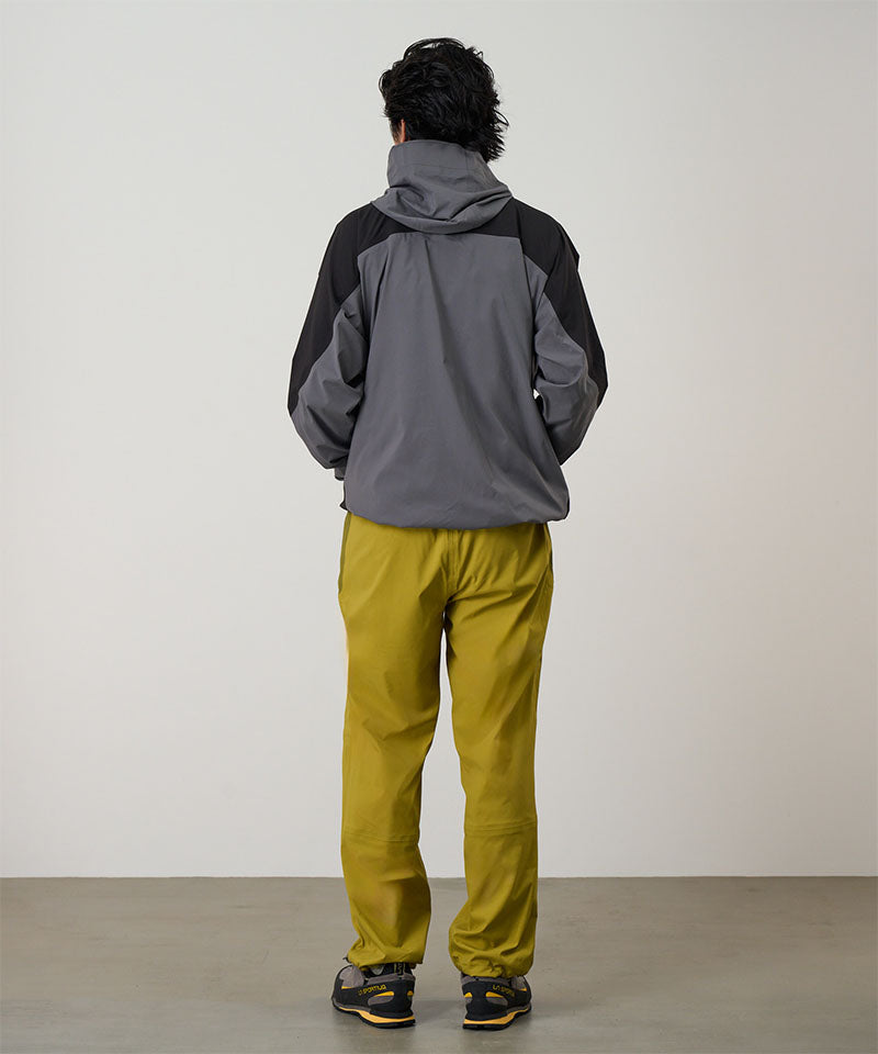 Person wearing a gray and black jacket with yellow pants against a light tone background