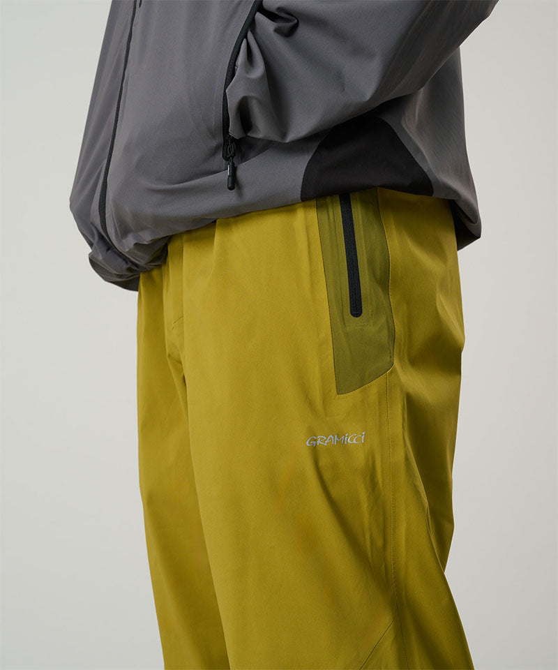 Person wearing a gray jacket and yellow pants with a brand logo on a light tone background