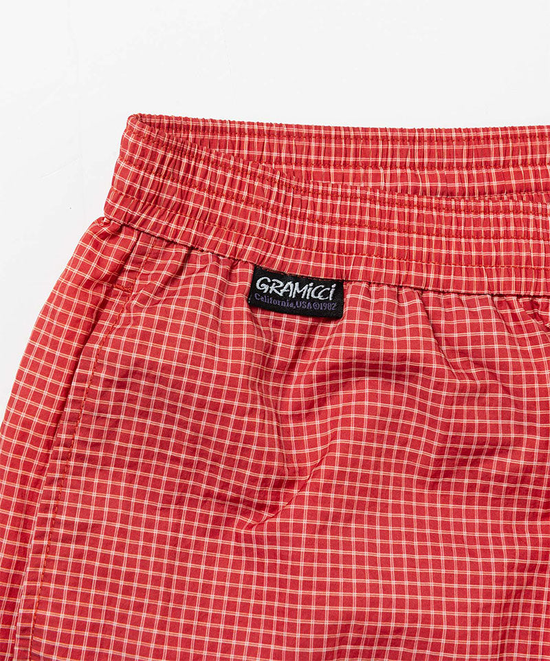 Front view close-up of red checkered Gramicci Grid Swim Shorts against a light-tone background.