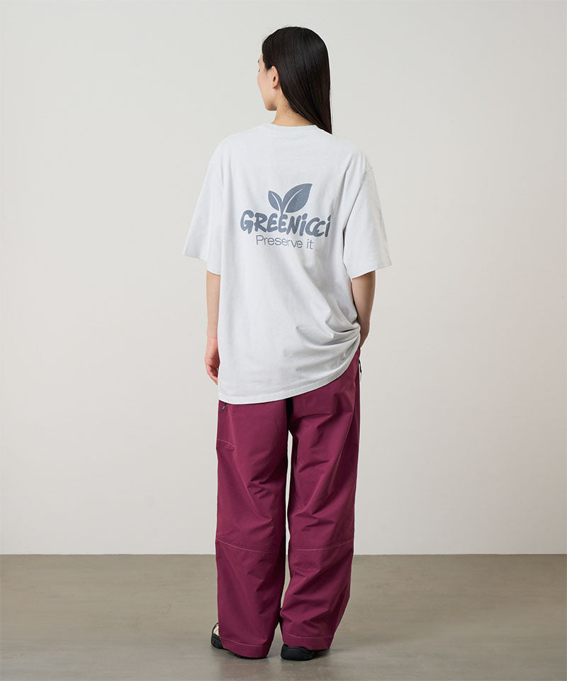 Back
view of a model wearing a smoke colored Gramicci Greenicci Tee with a graphic and purple pants on a light tone background.