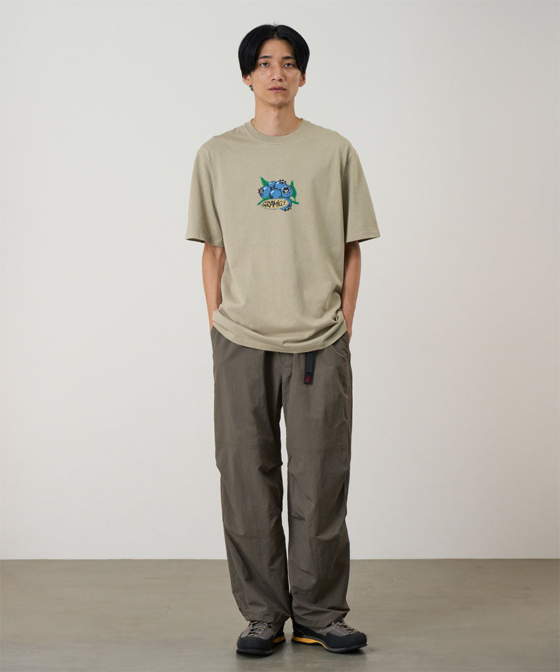 Model wearing a beige Gramicci Blueberry Tee featuring a blueberry graphic and brown shorts on a light tone background.