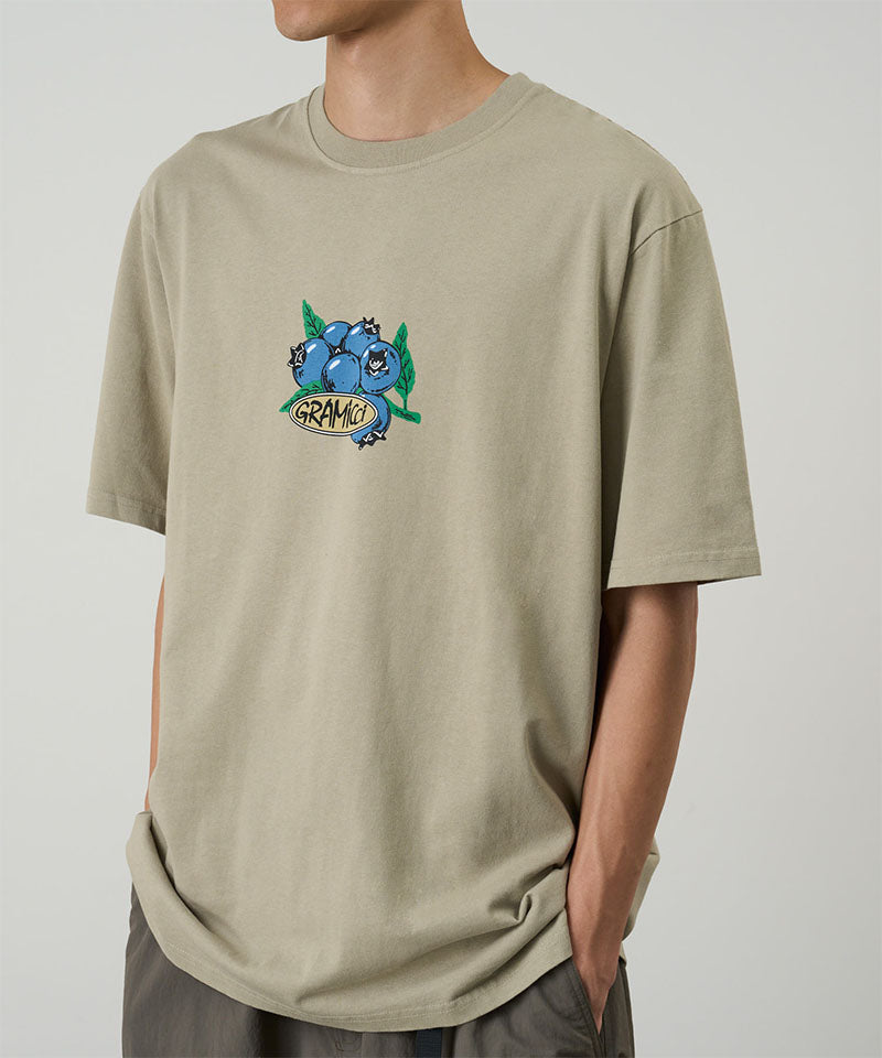 Model wearing a beige Gramicci Blueberry Tee featuring a blueberry graphic against a light tone background.