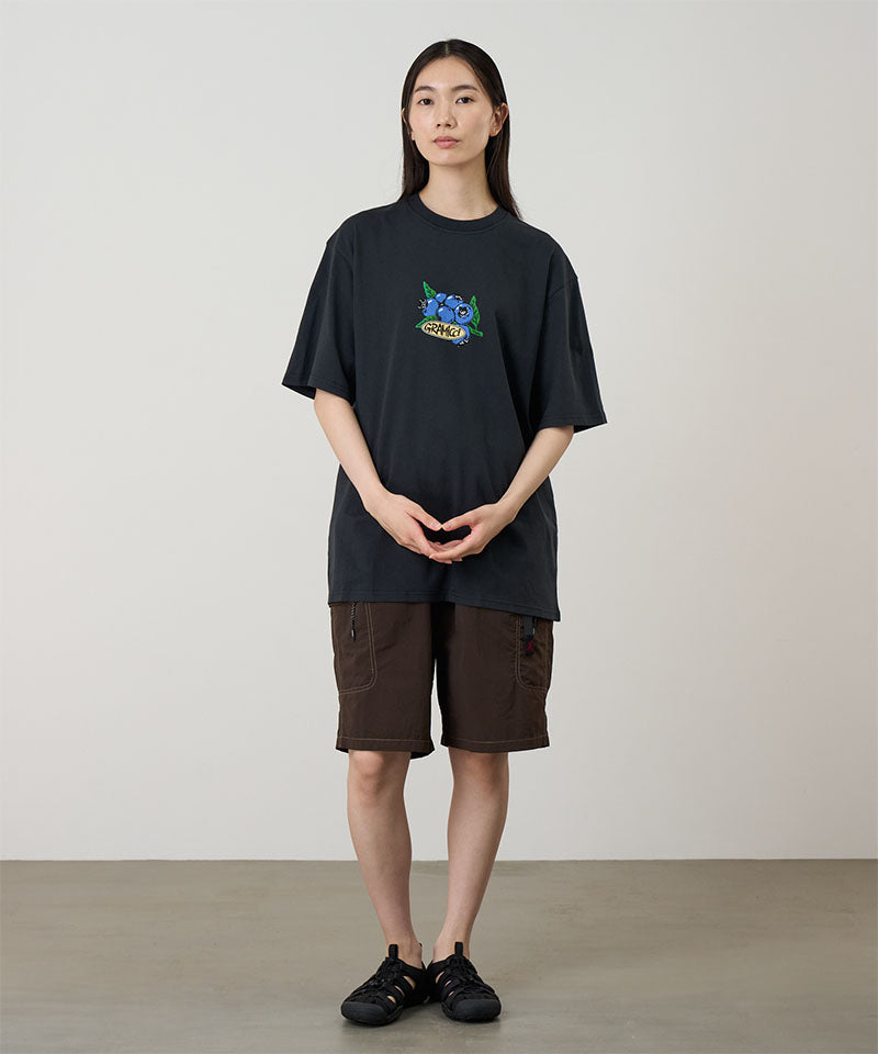 Model wearing a black Gramicci Blueberry Tee featuring a blueberry graphic and brown shorts on a light tone background.