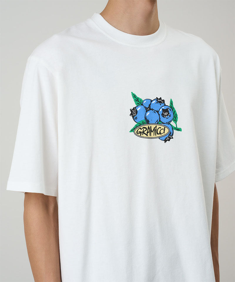 Model wearing a white Gramicci Blueberry Tee featuring a blueberry graphic against a light tone background.