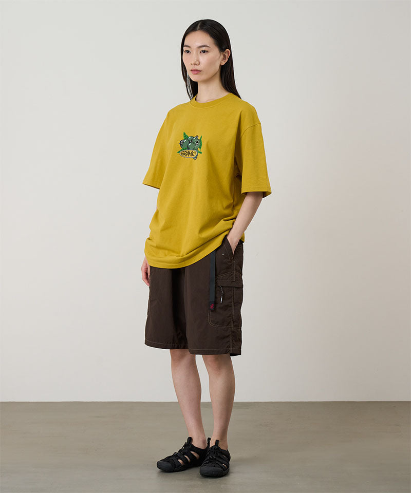 Model wearing a yellow Gramicci Blueberry Tee with a blueberry graphic and brown shorts on a light tone background.