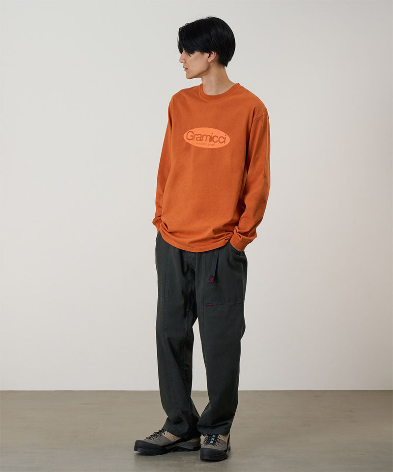 Model wearing a orange Gramicci Gramicci Outdoor Gear L/S Tee with a light orange graphic and dark pants on a light-tone background.