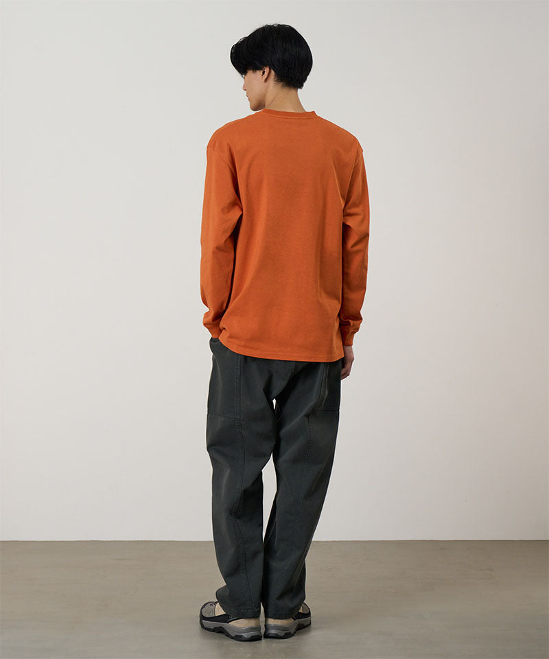 Back view of a model wearing a orange Gramicci Gramicci Outdoor Gear L/S Tee and dark pants on a light-tone background.