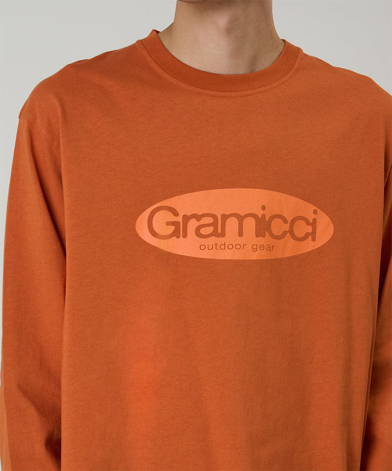 Model wearing a Gramicci orange Gramicci Outdoor Gear L/S Tee with a light orange graphic against a light-tone background.