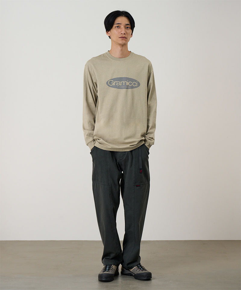 Model wearing a beige Gramicci Gramicci Outdoor Gear L/S Tee with a grey graphic and blue jeans on a light-tone background.
