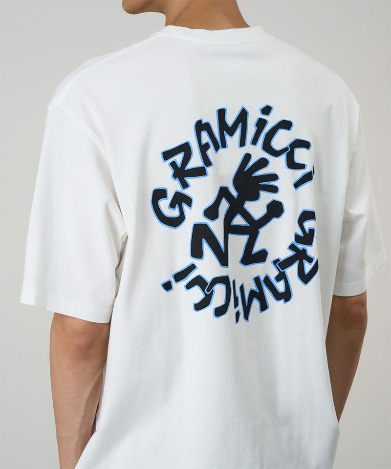Rear view of a model wearing a white Gramicci Running Man Tee with graphic on a light tone background.