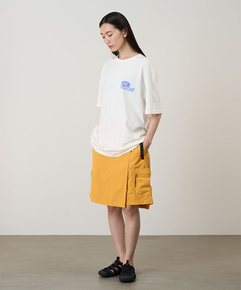 Model wearing a white Gramicci '82 Tee with a blue graphic and yellow skort on a light tone background.