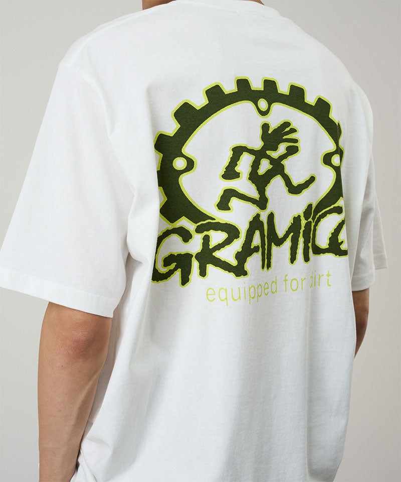 Back view of a model wearing a Gramicci white Equipped For Dirt Tee with a green graphic against a light-tone background.