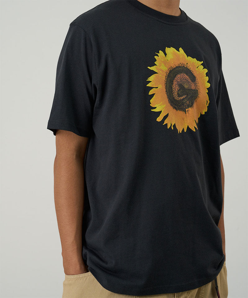 Model wearing a Gramicci vintage black G-Flower Tee with sunflower graphic against a light tone background.