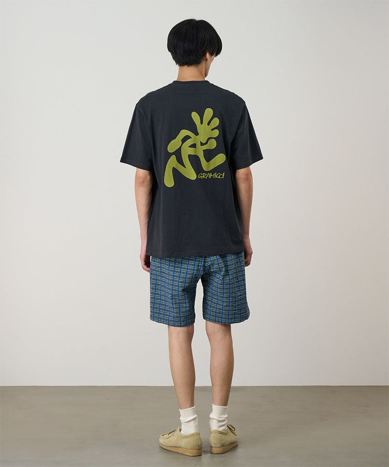 Person wearing a black t-shirt with green graphics and plaid shorts on a plain background