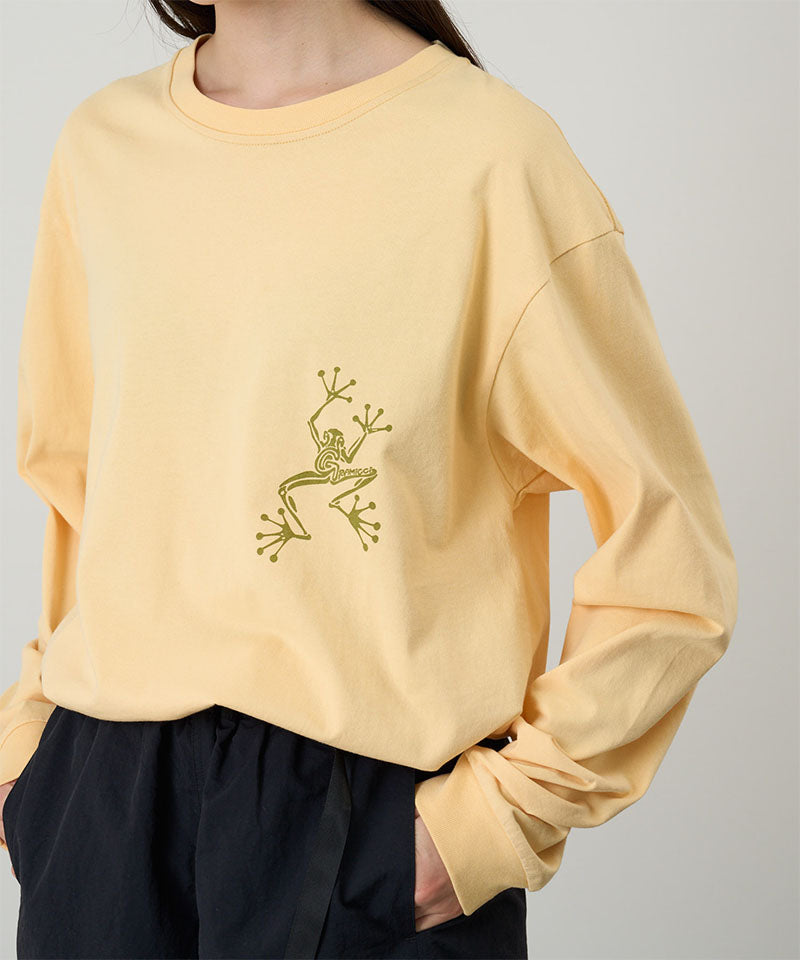 Model wearing a Gramicci mango colored Sticky Hands L/S Tee with green frog graphic against a light tone background.