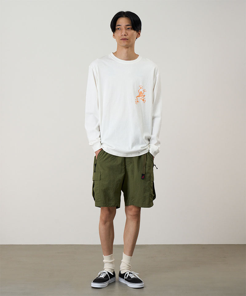 Model wearing a white Gramicci Sticky Hands L/S Tee with a orange frog graphic and olive shorts on a light tone background.