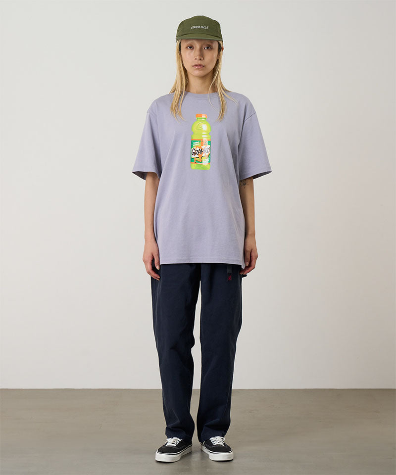 Model wearing a lavender Gramicci Quencher Tee with a hydration drink graphic and blue pants on a light tone background.